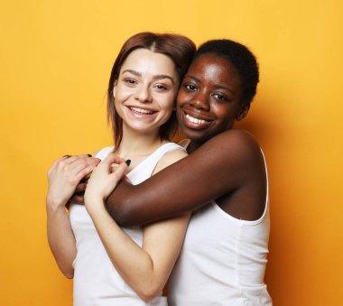 Genç, mutlu, çok kültürlü kadınlar yan yana durur ve sarı arka planda izole edilmiş kameraya gülümserler.