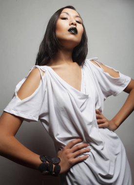 Gri arka planda siyah dudaklı, şık beyaz elbise giymiş güzel, seksi Asyalı kadın modeli.