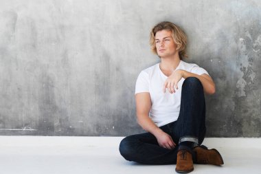 Kot pantolon giyen ve yerde oturan yakışıklı bir manken. Stüdyo moda portresi. Yaşam tarzı ve insan kavramı.