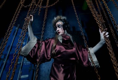 Parlak makyajlı genç bir kadın tenha bir manzarada ellerini kırmızı zincirlere uzatıyor..