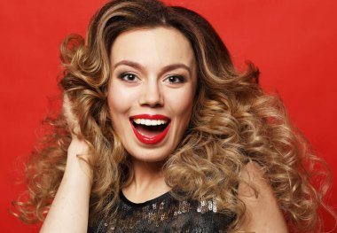 Yaşam tarzı, parti ve insan konsepti. Gece elbisesi giymiş sarışın kadın. Kırmızı arka planda oynaşan.