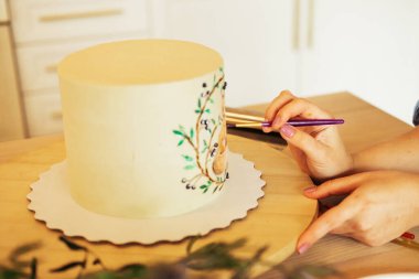 Yaşam tarzı, yemek pişirme ve serbest çalışma konsepti: Genç bir kadın pastayı süsler, fırçayla boyar.