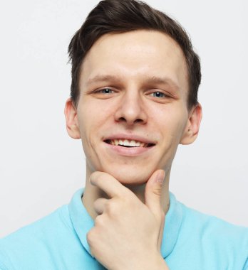 Yakışıklı genç adam gülümsüyor ve gri arka planda çenesine dokunuyor.