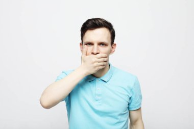 Ekose mavi gömlekli genç bir adam avuçlarıyla ağzını kapatıyor..