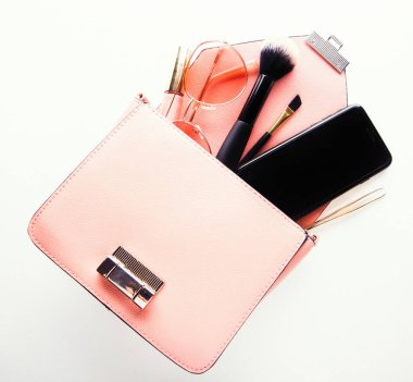 Düz deri kadın çantası beyaz arka planda kozmetik ve akıllı telefonla açılıyor. Moda ve güzellik.