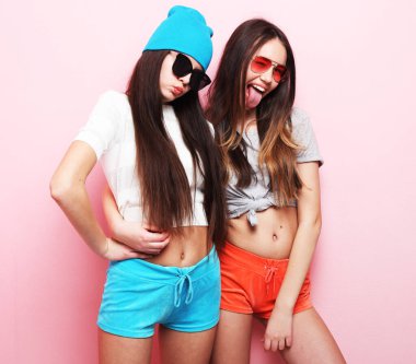 Yaşam tarzı ve insan konsepti: iki genç kız arkadaş bir arada duruyor ve eğleniyorlar. Kameraya bakıyorum. Pembe arkaplanda.