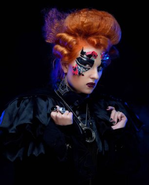 Cadı kostümü giymiş kızıl saçlı genç bir kadın. Maskeli balo için yaratıcı makyaj. Cadılar Bayramı ve parti konsepti.