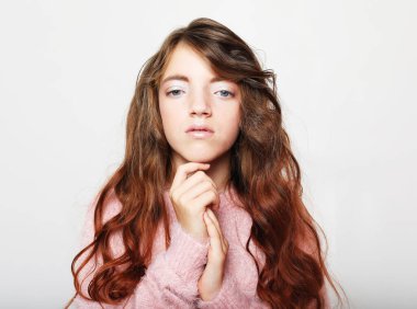 Yaşam tarzı, çocukluk, duygu ve çocuk konsepti: Gri arka planda izole edilmiş çenesine dokunmayı düşünen sevimli, sevimli, dalgalı saçlı kızın portresi