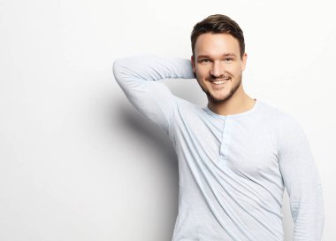 Yakışıklı, sıradan giyinmiş, beyaz arka planda kameraya bakan genç bir adam.