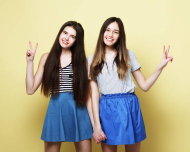 Yaşam tarzı ve insan konsepti: iki genç kız arkadaş bir arada duruyor ve eğleniyorlar. Kameraya bakıyorum. Sarı arkaplan..