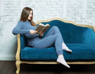 Genç sarışın kadın evde dinleniyor ve kitap okuyor.