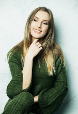 Uzun saçlı, yeşil örgü takım elbiseli, gevşemiş ve evinde dinlenen genç sarışın kadın..