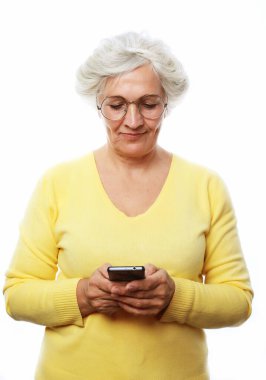 Beyaz arka planda dikilip modern akıllı telefon kullanırken neşeli bir şekilde gülümseyen ve kameraya bakan hoş, son sınıf güzeli bayan. Yaşam tarzı ve tehnoloji konsepti.