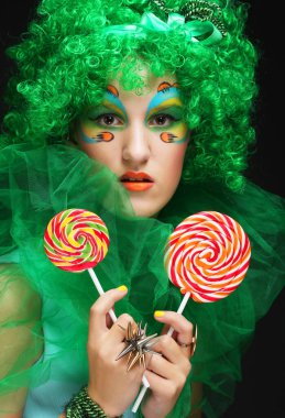 Lolipopu olan yaratıcı görünüşlü genç bir kadın. Parti ve karnaval. Parlak peruk.