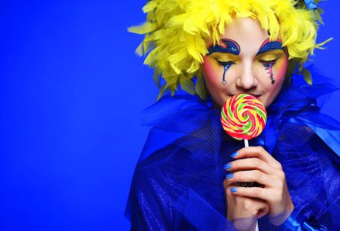 Lolipopu olan yaratıcı görünüşlü genç bir kadın. Parti ve karnaval. Parlak peruk. Kapat..