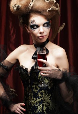 Parti, tatil ve Cadılar Bayramı konsepti. Cadı kostümlü, parlak makyajlı ve kıvırcık saçlı güzel bir kadın elinde bir bardak şarap tutuyor..