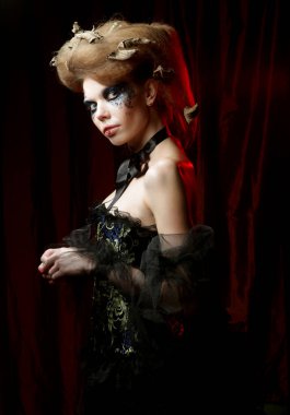 Cadılar Bayramı ve parti konsepti. Güzel Gotik Prenses. Siyah elbiseli, yaratıcı makyajlı ve koyu kırmızı arka planda saç stili olan genç bir kadın..