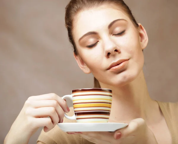 Beautiful woman drinking coffee. Photo of young blond girl holding a cup with coffee over beige background. Close up.