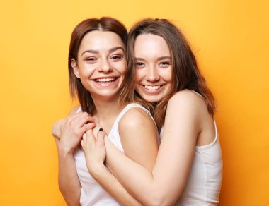 Arkadaşlık, duygu ve mutlu insanlar konsepti. Sarı arka planda sarılan iki gülen kız.