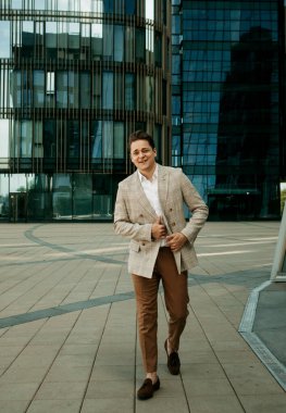 Takım elbiseli mutlu genç bir adam bir yaz günü modern bir iş merkezinin yakınında poz veriyor.