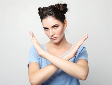 lifestyle, body language, emotion and people concept. Young brunette woman wearing casual style rejection expression crossing arms doing negative sign, angry face over grey background.