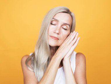 Parmaklarını çenesine dayamış düşünceli yaşlı kadın güzel anıları anımsıyor ve sarı arkaplanda portreyi kapatıyor.