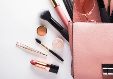 Flat lay of pink leather woman bag open out with cosmetics over white background. Fashion and beauty.