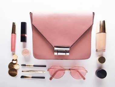 Flat lay of pink leather woman bag open out with cosmetics over white background. Fashion and beauty.