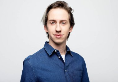 Yaşam tarzı, duygu ve insan konsepti: yakışıklı genç adam gri arka planda kameraya bakarken mavi gömlek giyiyor