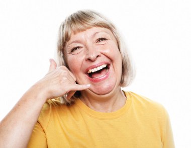 İletişim, vücut dili ve yaşlılar konsepti: Beyaz arka plan üzerinde duran sarı gömlekli yaşlı kadın telefonla el ve parmak hareketleriyle telefonla konuşuyor gibi..