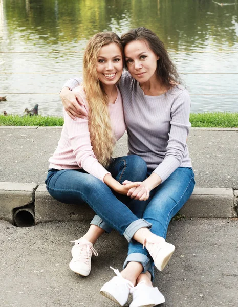Mutter und ihre erwachsene Tochter sitzen auf der Straße am See, glückliche Familie, schöne Frauen — Stockfoto