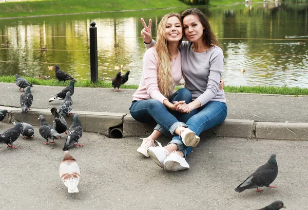 Mamá y su hija adulta están sentadas en el camino cerca del lago, familia feliz, mujeres hermosas — Foto de Stock