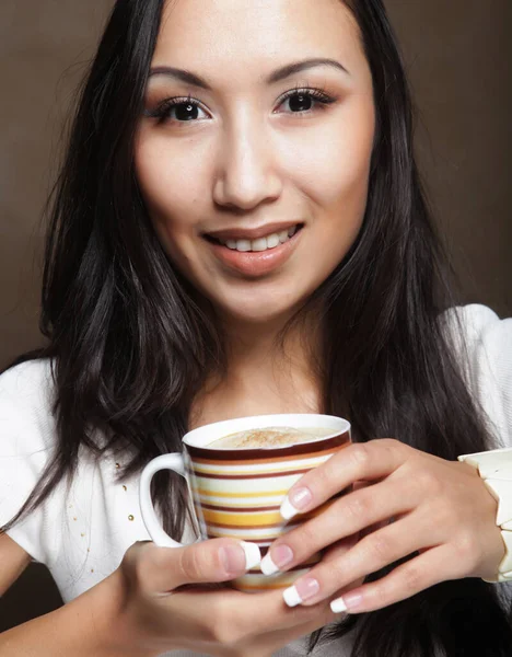 Młoda ładna azjatycka kobieta pije kawę, trzymając filiżankę na beżowym tle. — Zdjęcie stockowe