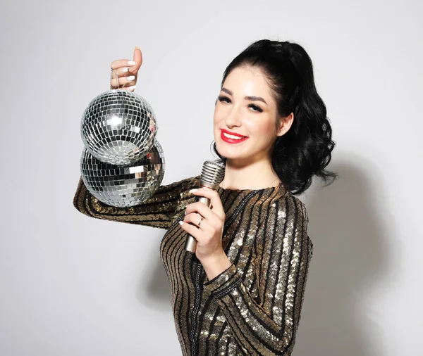 Jovem mulher em vestido de noite segurando microfone e bola de discoteca. Brighrt compõem e penteado ondulado. — Fotografia de Stock