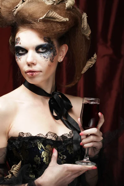 A beautiful woman in a witch costume with bright makeup and curly hair is holding a glass of wine. — Stock Photo, Image