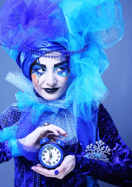 Mujer joven con rostro creativo y traje que sostiene el reloj despertador sobre fondo azul. —  Fotos de Stock