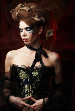 Yaratıcı makyajlı ve koyu kırmızı arka planda saç stili olan genç bir kadın..