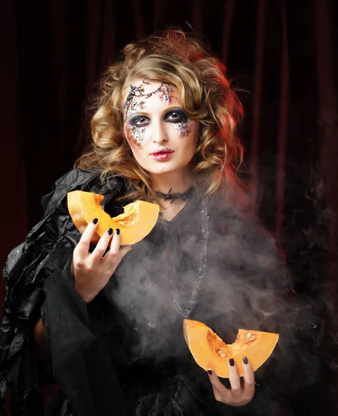 Ung vacker kvinna i en häxa kostym med ljusa makeup och frisyr håller en pumpa, en symbol för halloween. Fest. Semester. Karneval. — Stockfoto