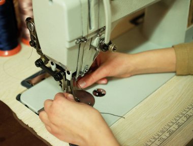 Genç bir kadın deri çanta dikiyor.