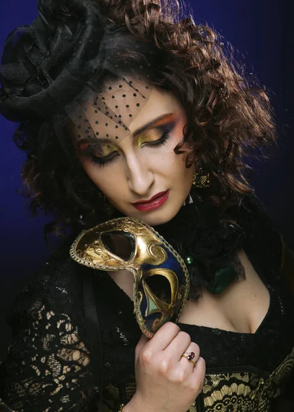 Красивая молодая женщина с ярким макияжем и шляпой с вуалью, держащая венецианскую маску — стоковое фото