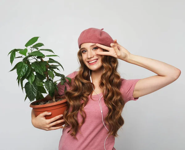 Smiling woman with long wavy hair wearing pink clothes, standing over grey background and holding flower in pot — Stock Photo, Image