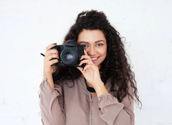 Portrait of Afican woman holding digital photocamera and laughing over white background in studio.