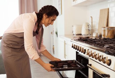 Genç esmer kadın fırından kek tepsisi alıyor..