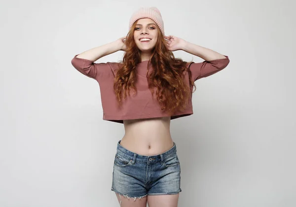 Schöne junge glückliche Frau mit rosa Hut und Jeanshosen über grauem Hintergrund — Stockfoto