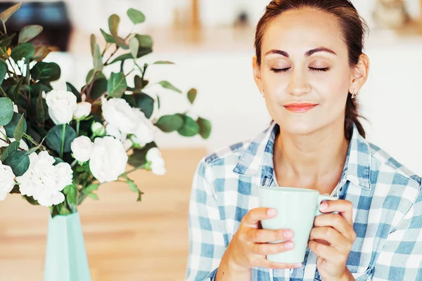 Молода жінка посміхається і тримає чашку кави або чаю, насолоджується хорошим ранком . — стокове фото