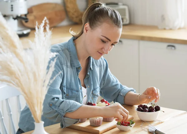 Young woman pastry chef decorates cupcakes with berries — Stock Photo, Image
