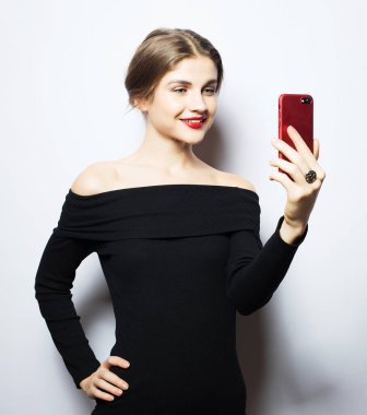 Selfie zamanı. Genç, gülümseyen sarışın kadın beyaz arka planda özçekim yapıyor..