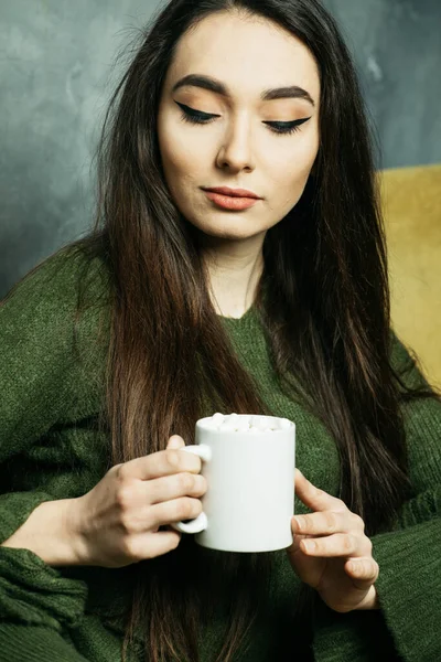 Красива молода жінка тримає чашку кави і сидить на стільці вдома. Стиль життя і концепція людей . — стокове фото