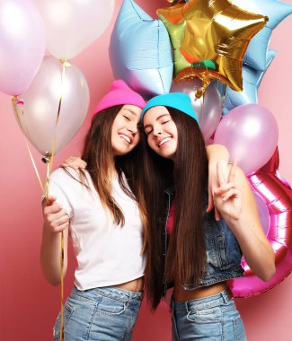 İki güzel duygusal kız balonları tutuyor ve rozete karşı poz veriyor.