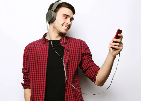 Mladý muž nosí sluchátka a drží mobilní telefon. — Stock fotografie
